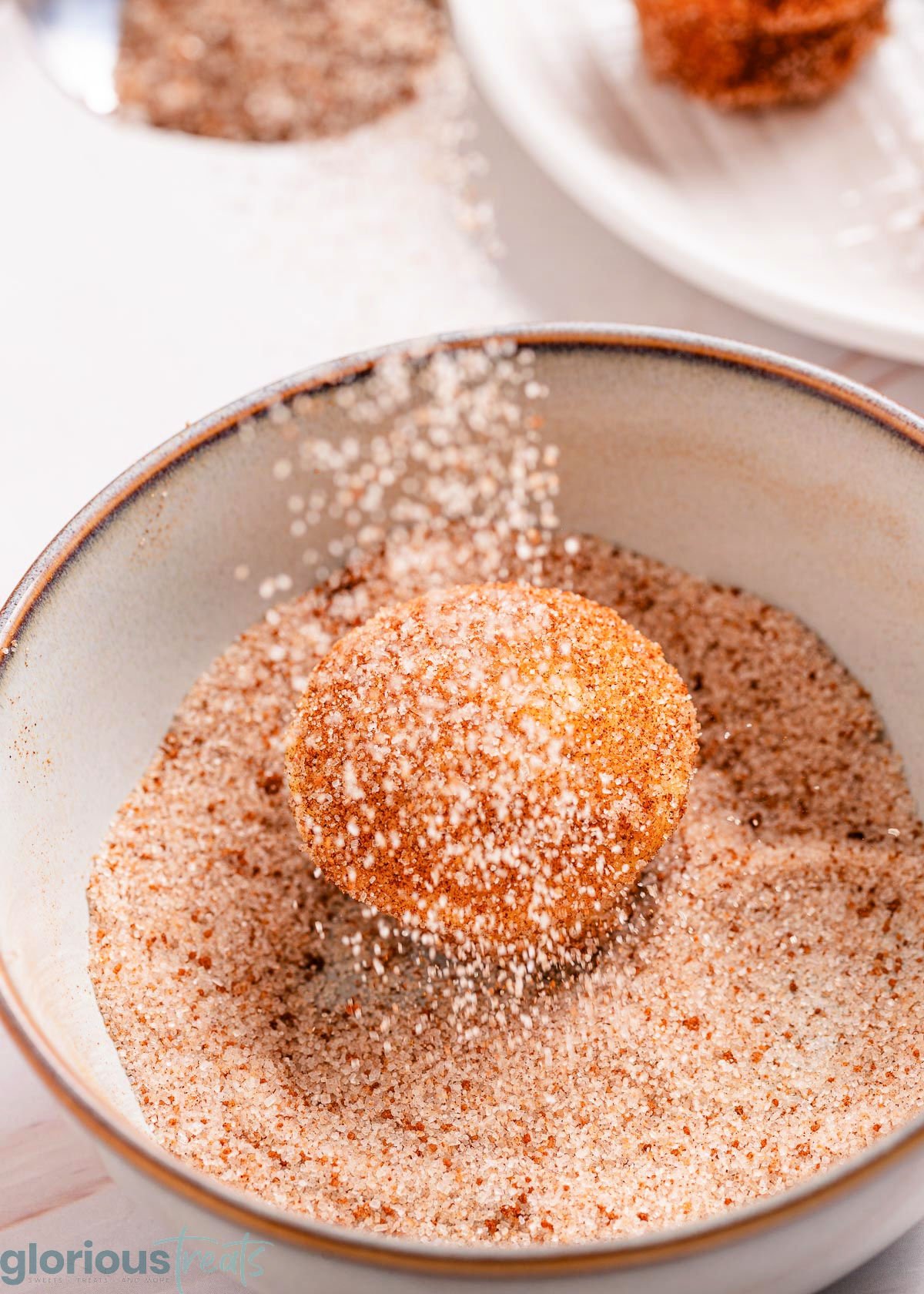 muffin in a bowl being tossed with cinnamon and sugar.