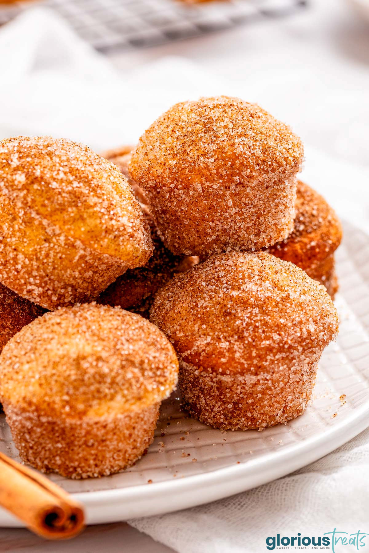 white plate full of cinnamon sugar donut muffins in a pile with a cinnamon stick on the plate.
