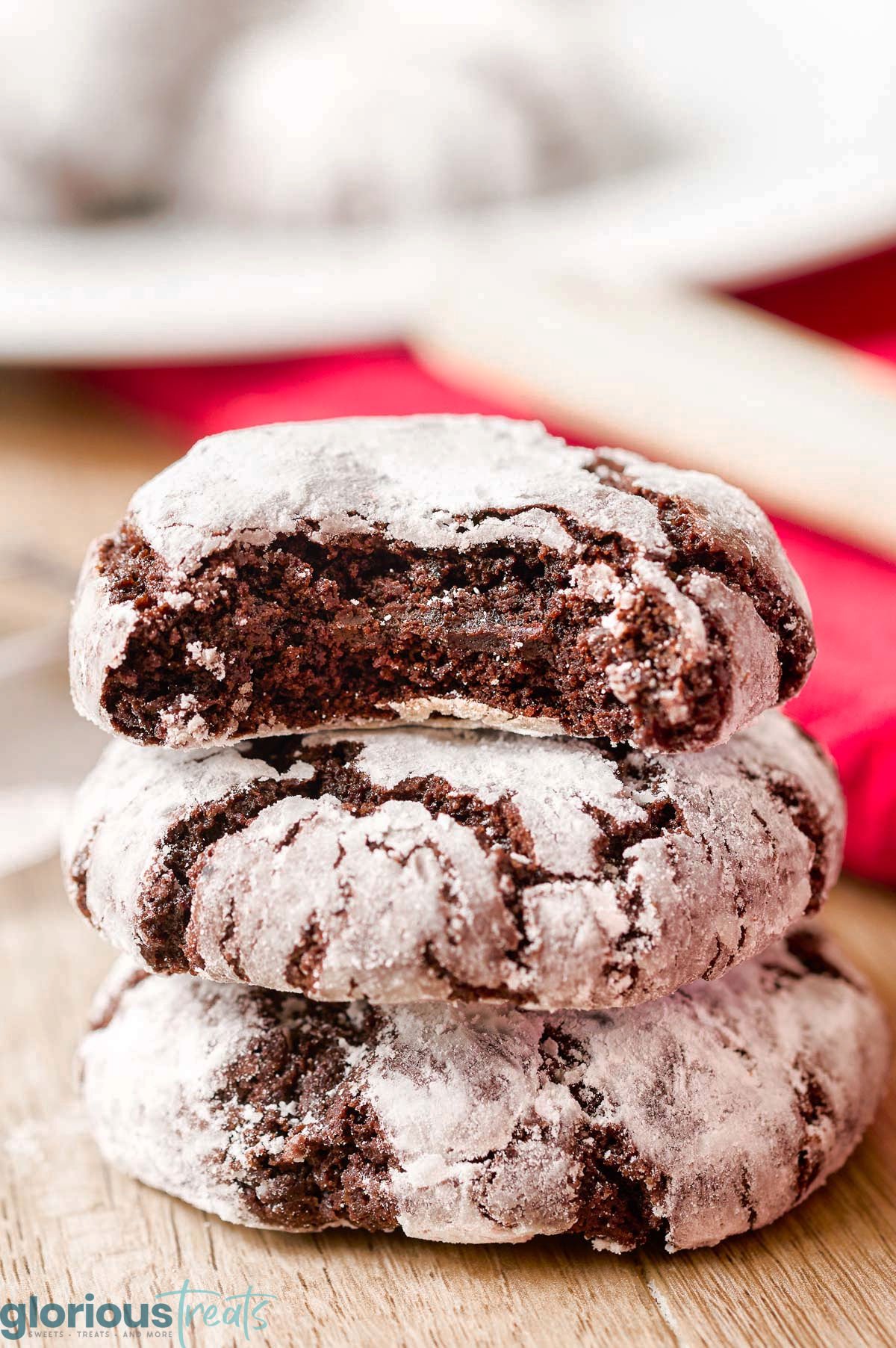three chocolate crinkle cookies stacked on top of each with top cookie having a bite removed.