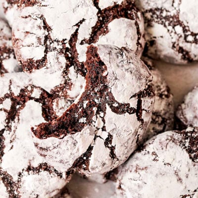 top down look at chocolate crinkle cookies with the classic powdered sugar finish. top cookie has a bite taken out of it.