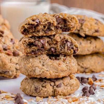 three cowboy cookies stacked on top of each other with the top cookie split in half so you can see the melted chocolate.