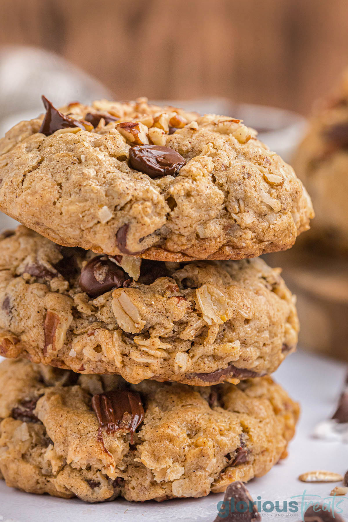 three cowboy cookies stacked on a white marble surface with chocolate chips scattered about.