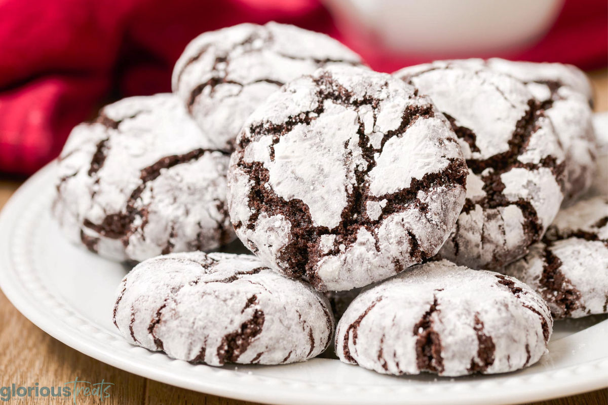 white plate topped with about seven chocolate cookies covered in powdered sugar. red napkin in the background.