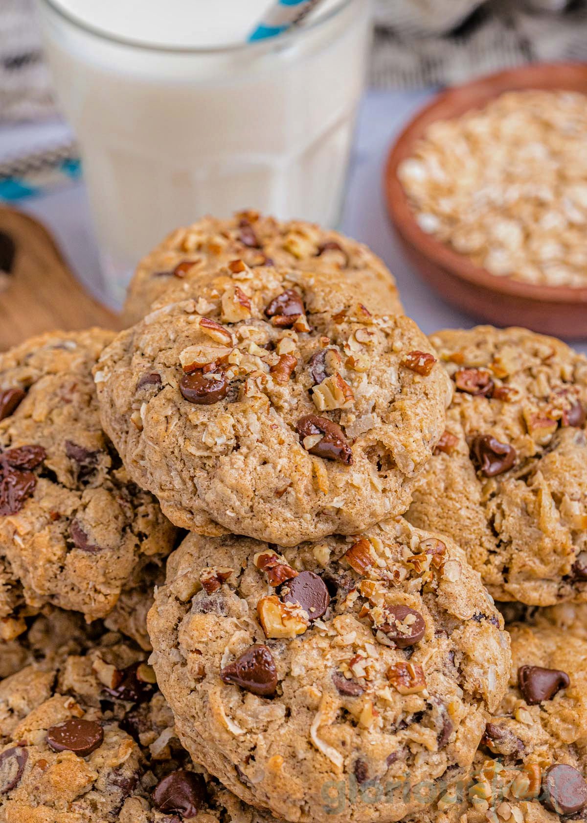 top down look at a plate of cowboy cookies piled high. a glass of milk can be seen in the background.