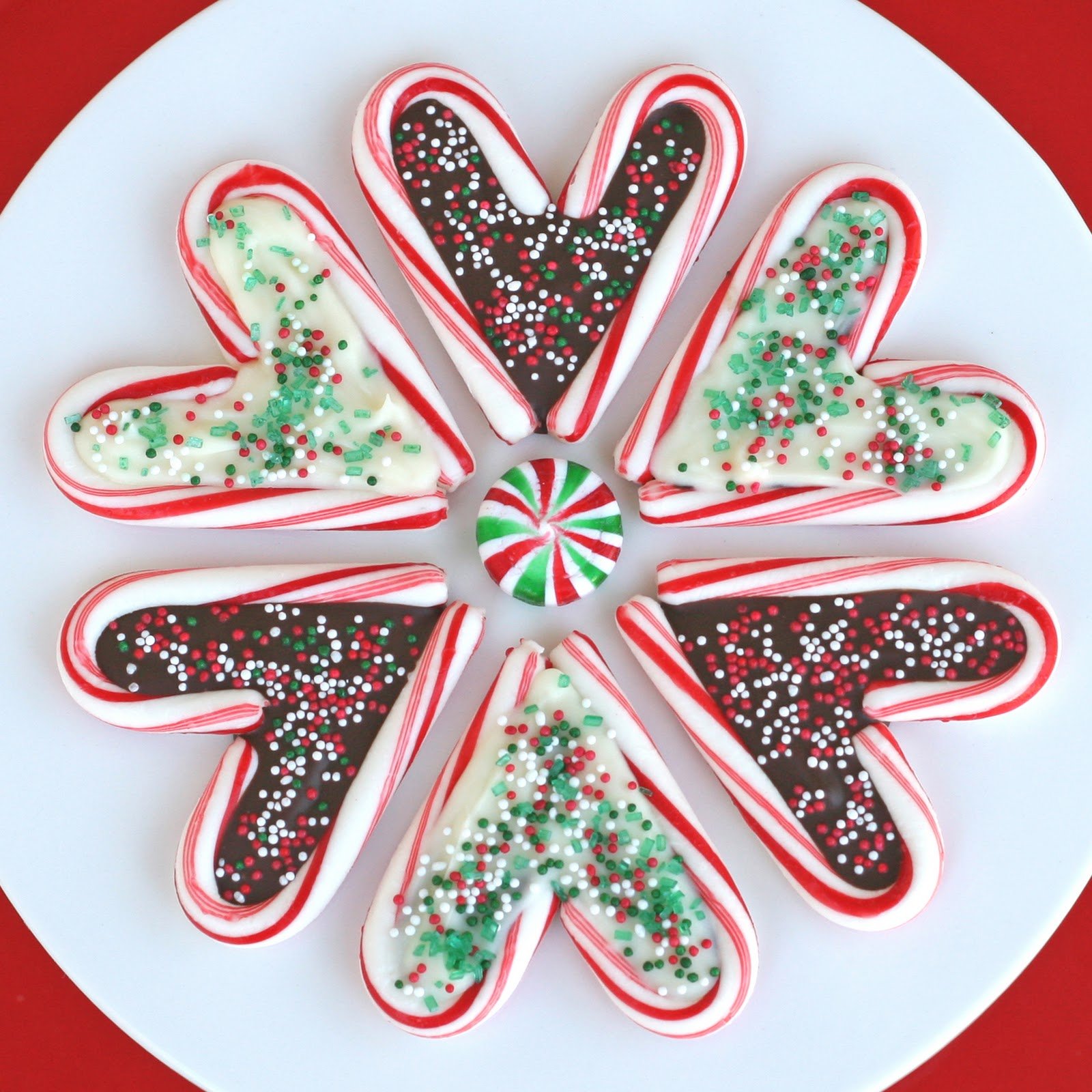 hearts made from candy canes and melted chocolate and decorated with christmas sprinkles sitting on a white plate.