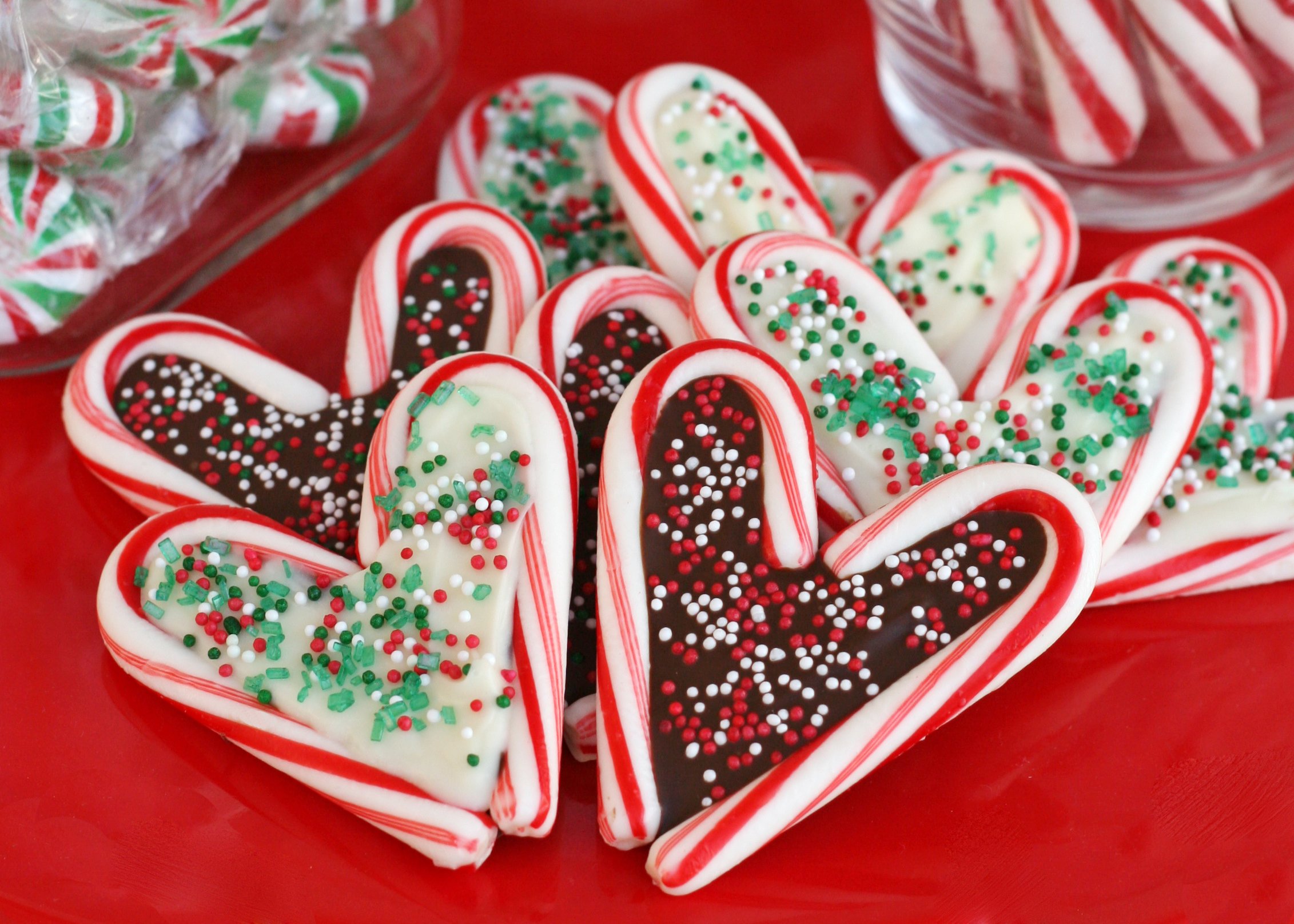 candy cane hearts with chocolate centers and decorated with sprinkles sitting on red surface.