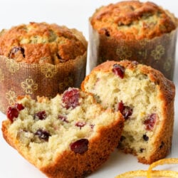 cranberry orange muffin split in half with orange peel text two whole muffins in background