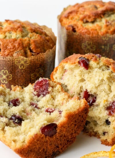 cranberry orange muffin split in half with orange peel text two whole muffins in background