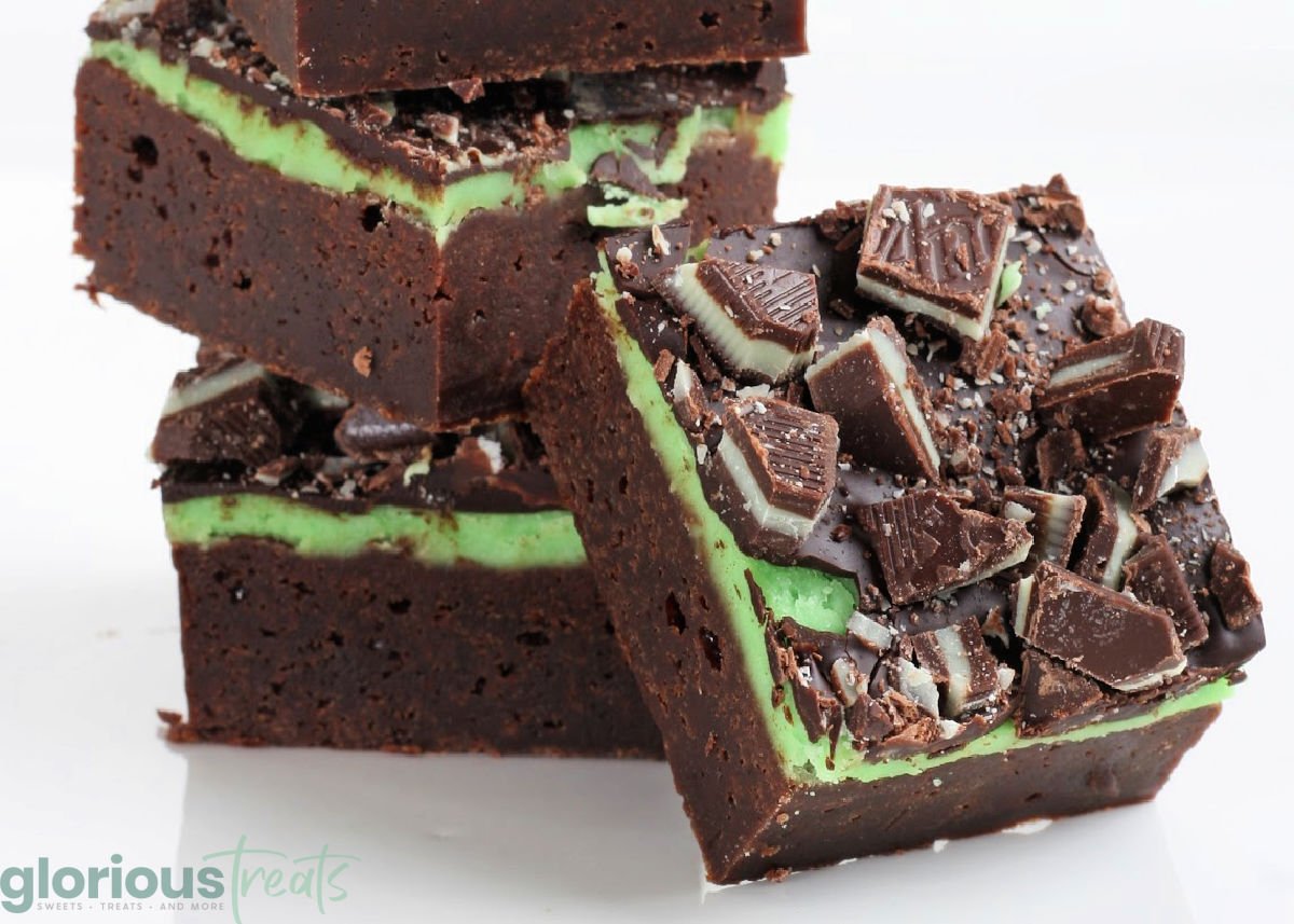 three mint brownies stacked with one brownie leaning against the stack. the entire background is white.