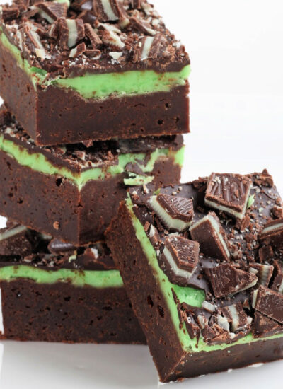 three mint brownies stacked with one brownie leaning against the stack. the entire background is white.