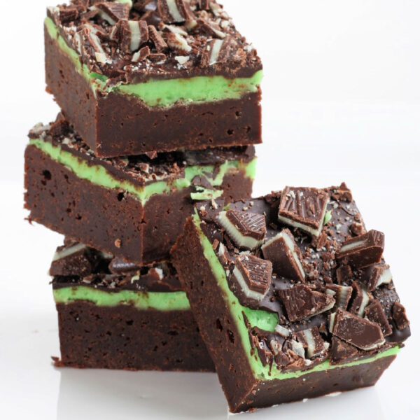 three mint brownies stacked with one brownie leaning against the stack. the entire background is white.