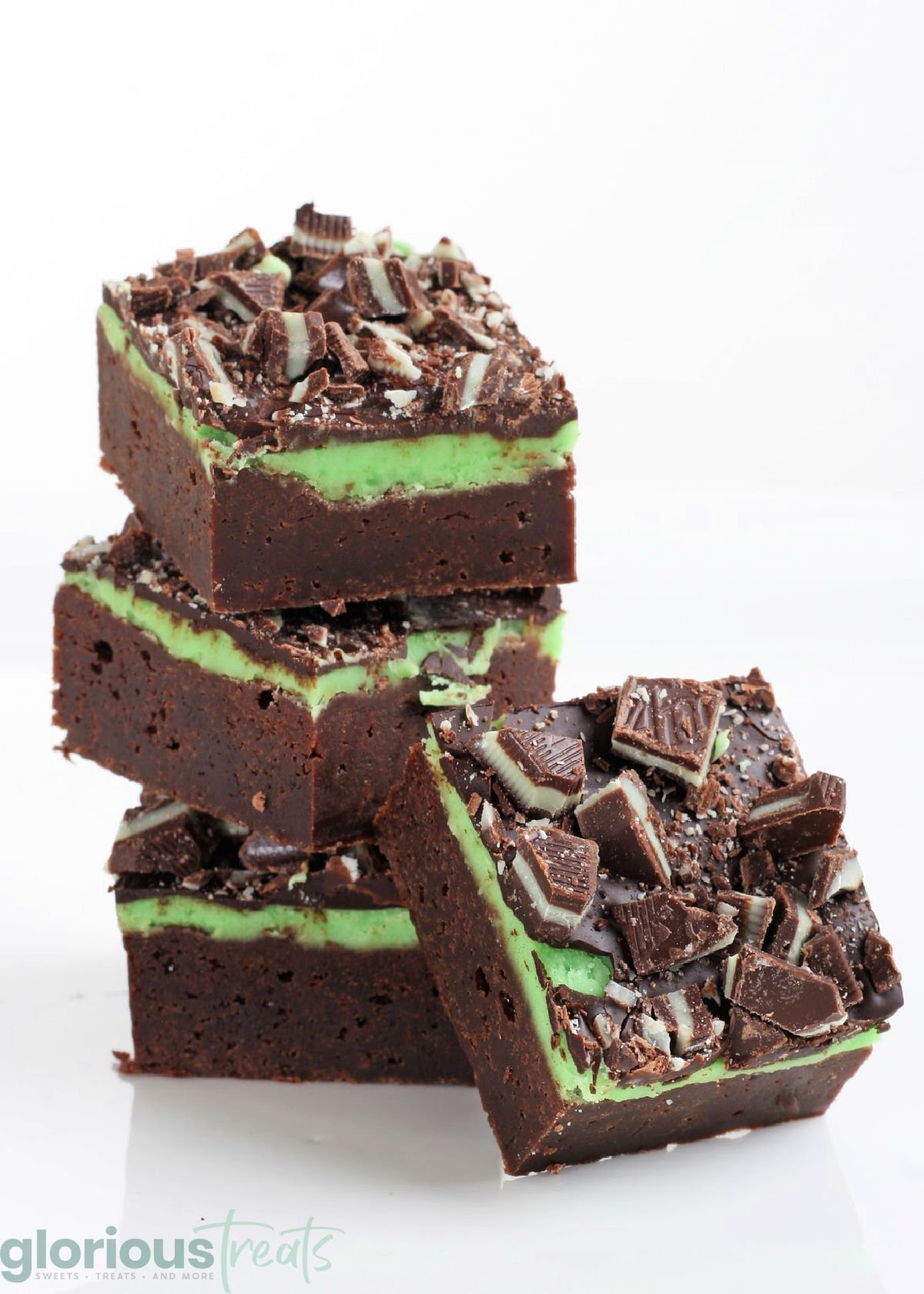 three mint brownies stacked with one brownie leaning against the stack. the entire background is white.