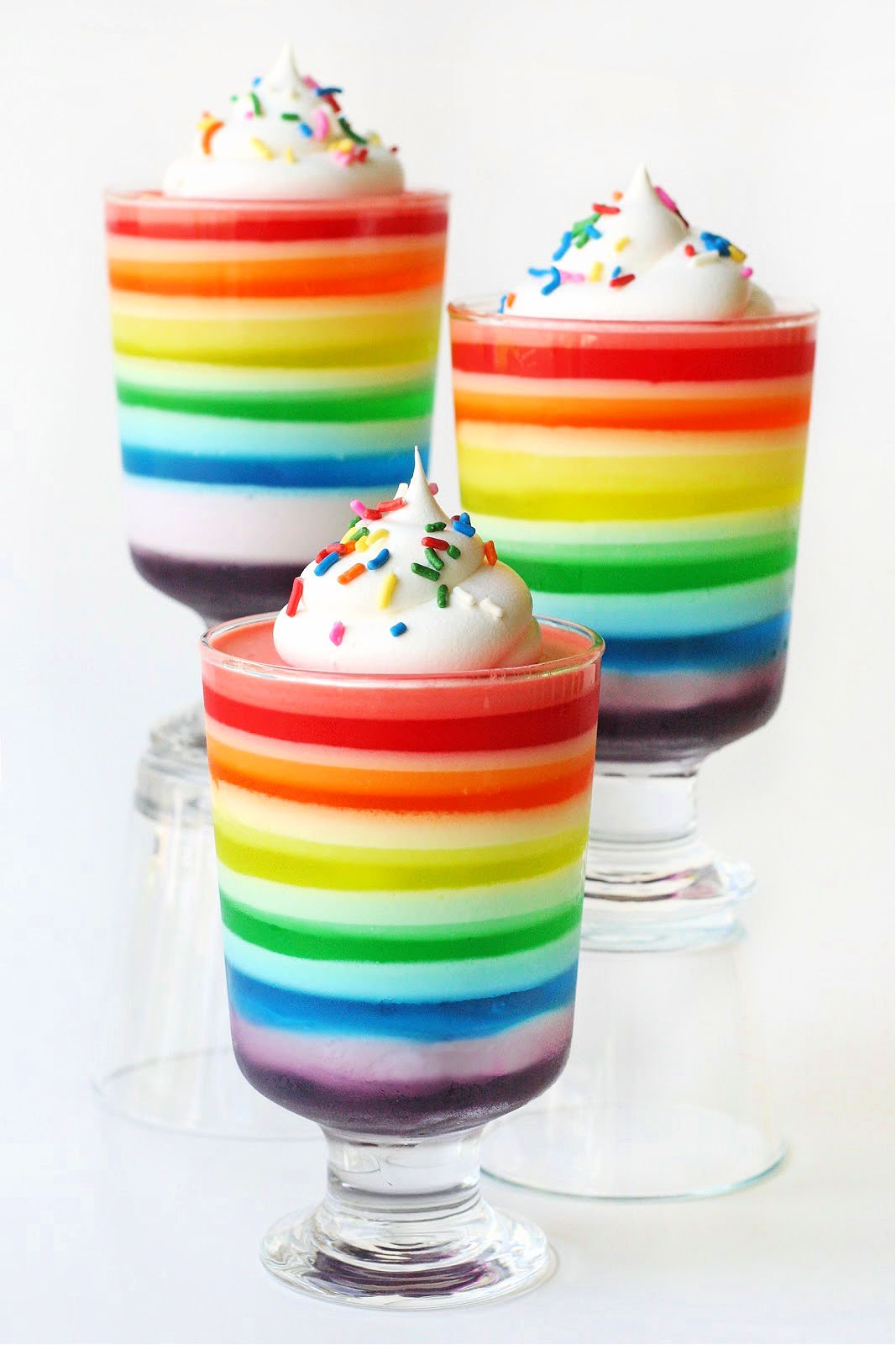 rainbow jello in 4 glasses topped with whipped cream and sprinkles