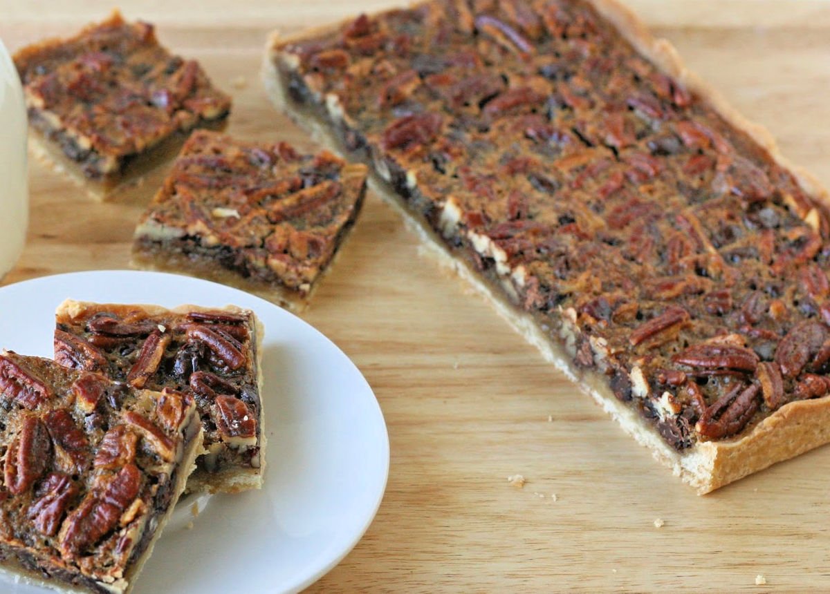 pecan pie bars cut into squares and about half of the slab sitting to the side still needing to be cut.