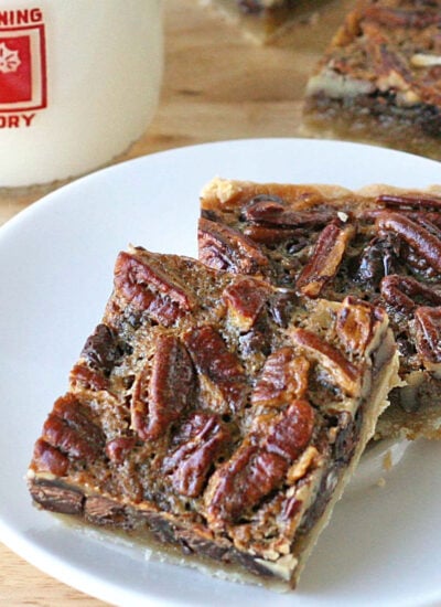 two pecan pie bars with chocolate chips sitting on small white plate in front of a glass of milk.