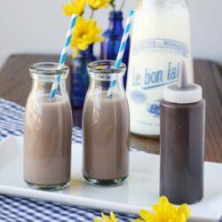 chocolate milk in glasses next to chocolate syrup in bottle