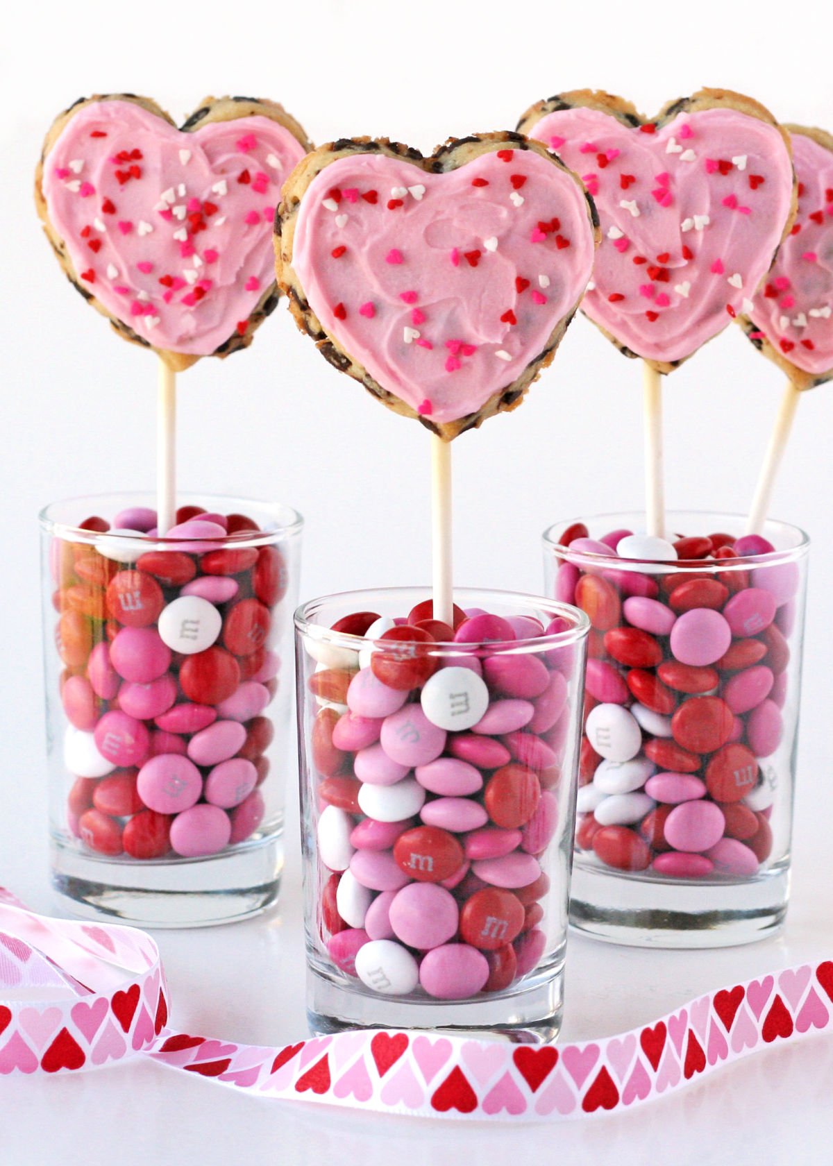 heart shaped chocolate chip cookies on sticks in cups with candy