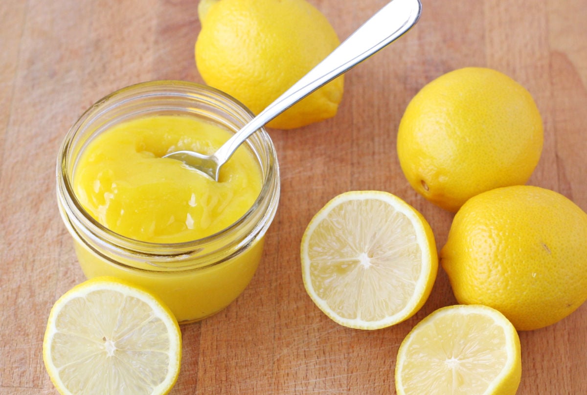 lemon curd in small jar with lemons on the side on wood board