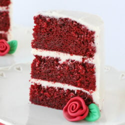 slice of red velvet cake with fondant rose on white plate square