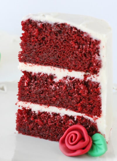 slice of red velvet cake with fondant rose on white plate square
