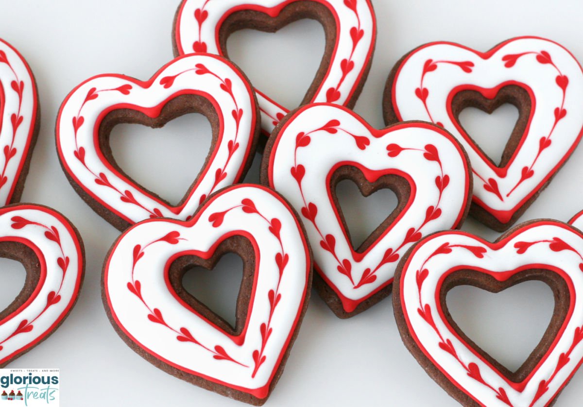 top down view of large white plate topped with chocolate cookies cut into heart shapes and decorated with royal icing.
