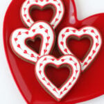 four chocolate heart cookies decorated with hearts made with royal icing.