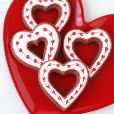 four chocolate heart cookies decorated with hearts made with royal icing.
