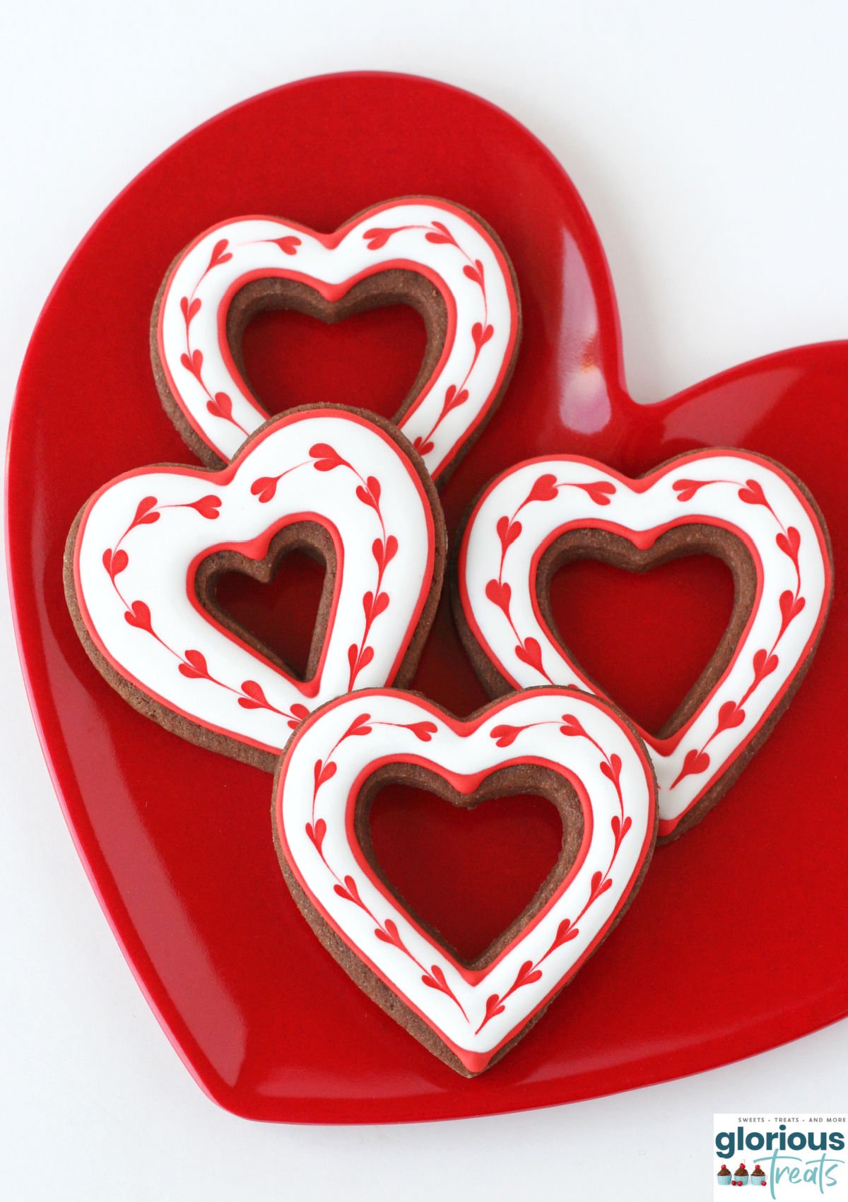 four chocolate heart cookies decorated with hearts made with royal icing.