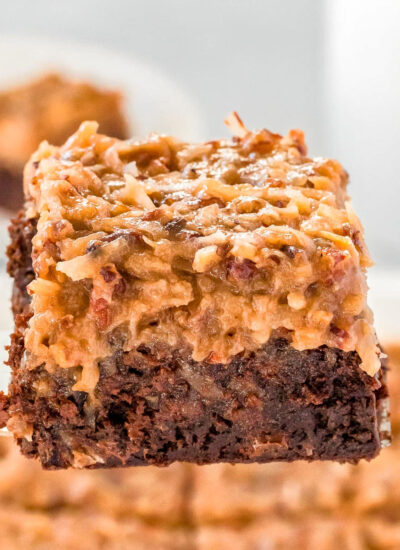 german chocolate brownie being held up with a server over the baking dish full of more brownies.