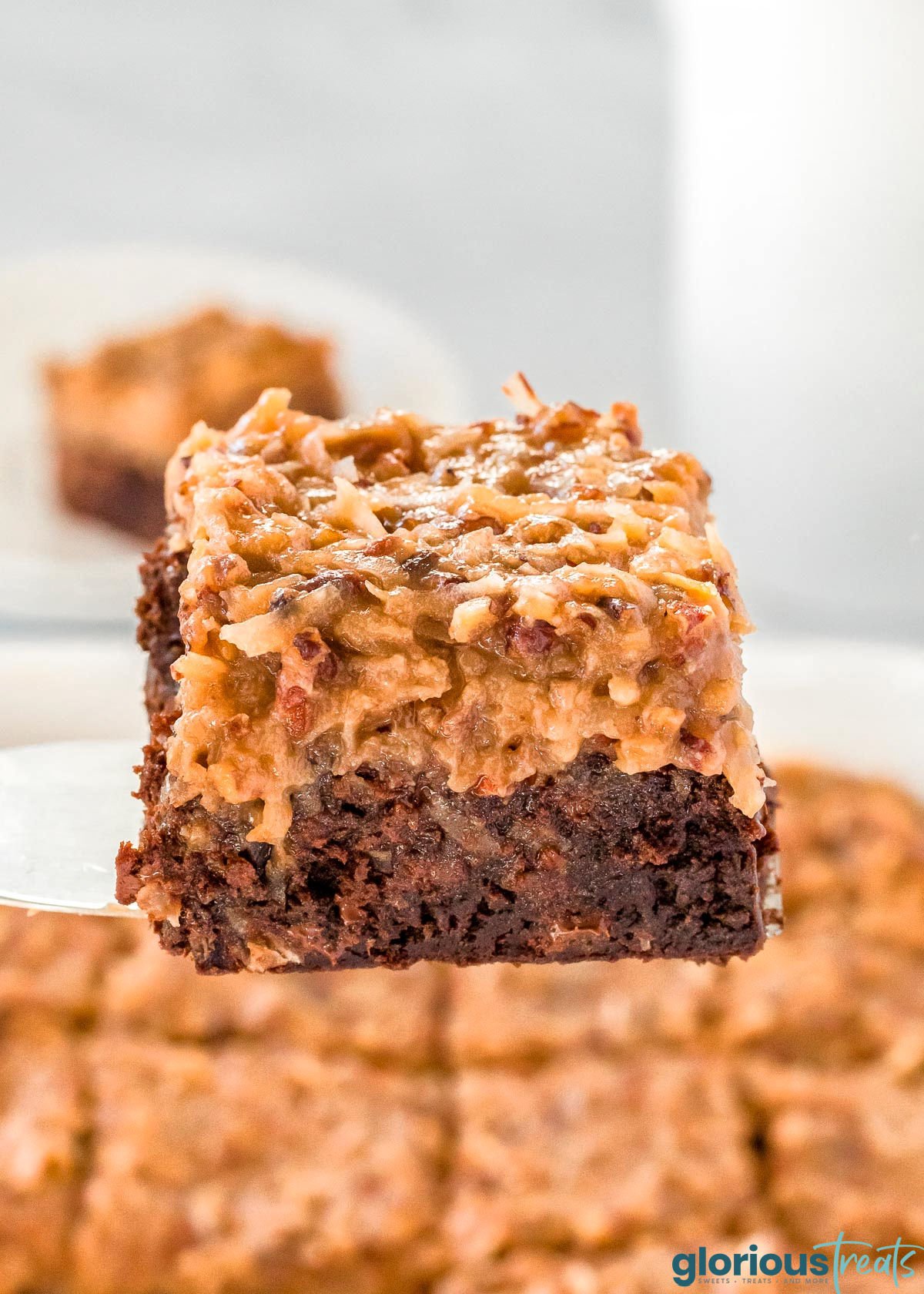 german chocolate brownie being held up with a server over the baking dish full of more brownies.