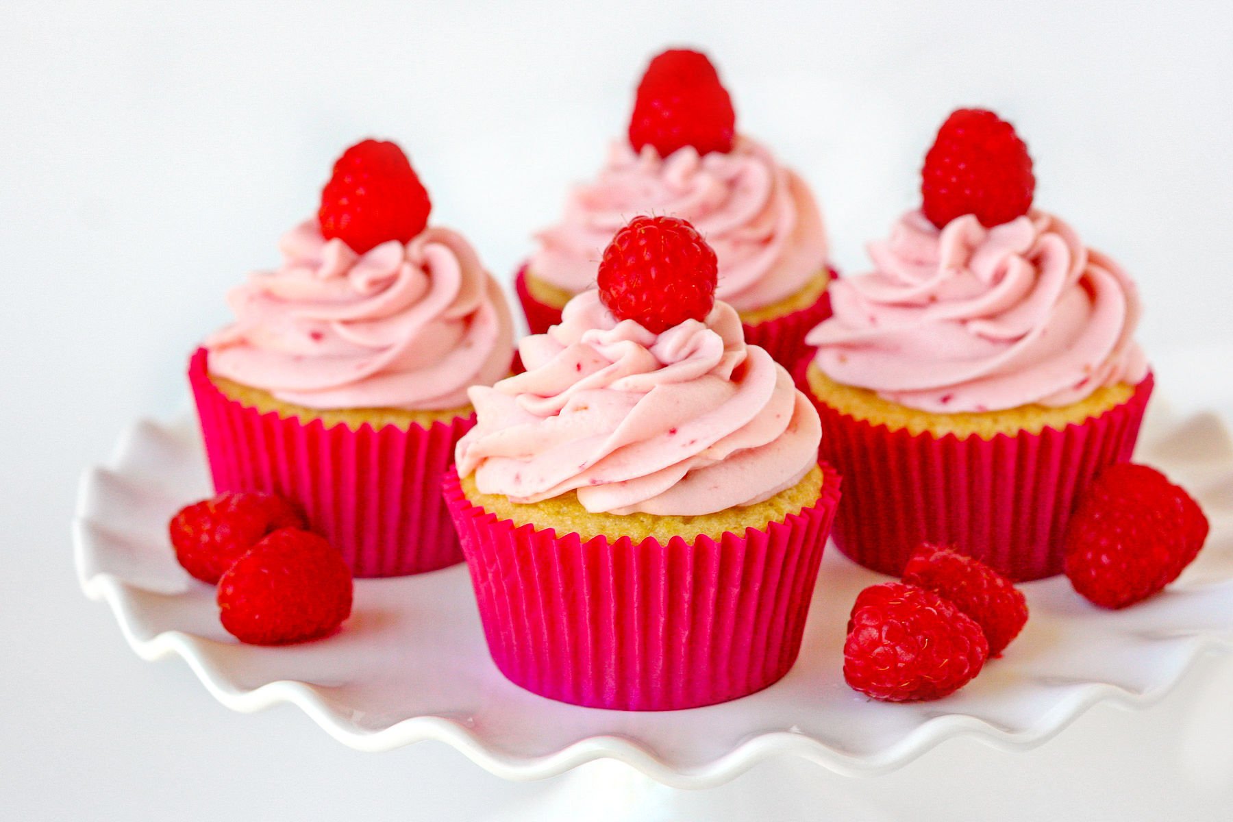 raspberry vanilla cupcakes with raspberry cream cheese frosting on white cake stand