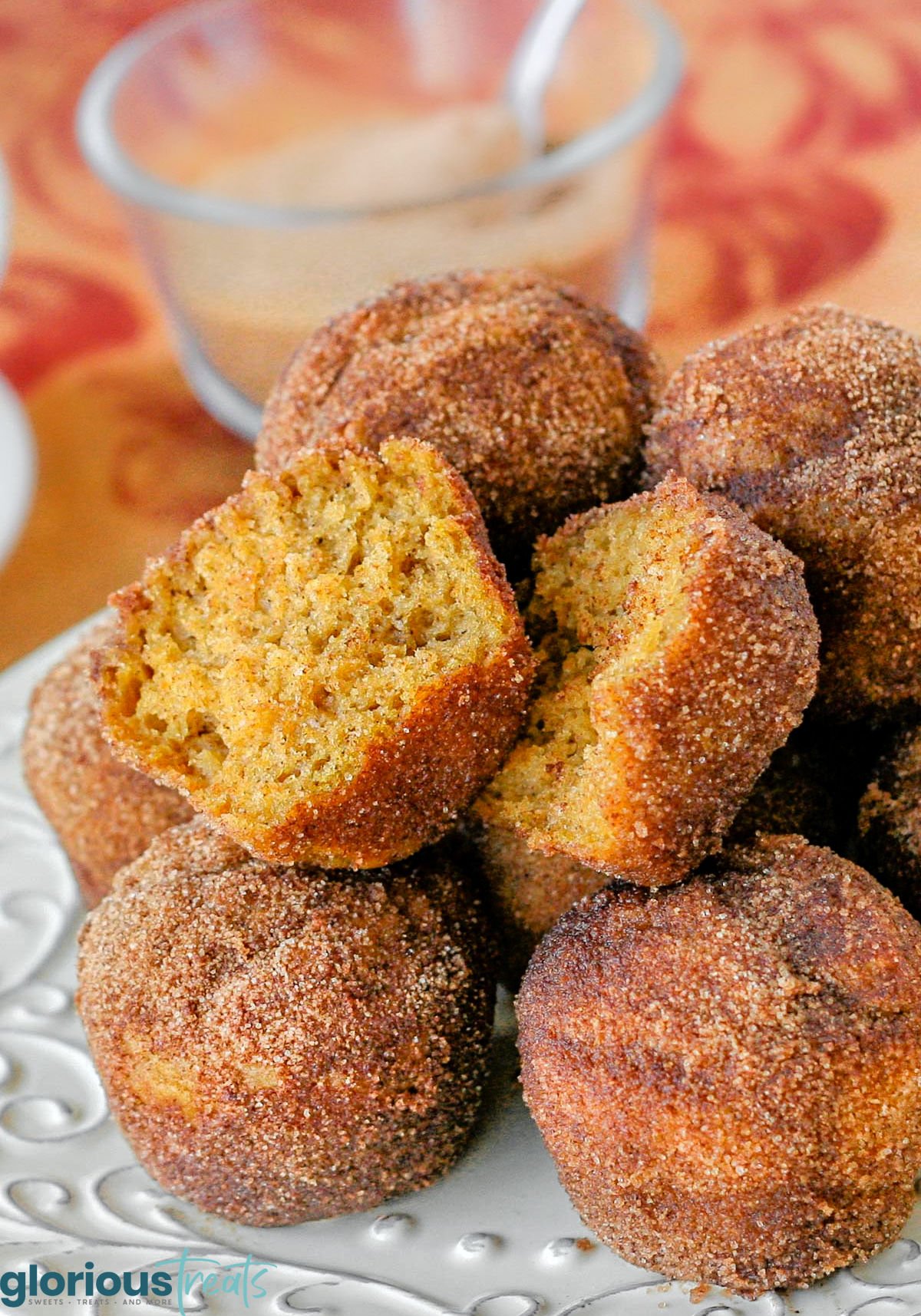 white metal pate is topped with a mound of pumpkin mini muffins rolled in cinnamon sugar so they look like donut holes. top muffin has been torn in half.