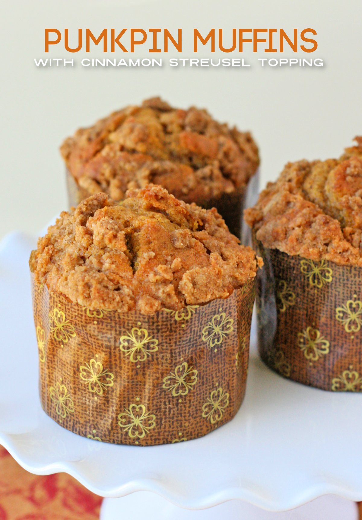 three pumpkin muffins recipe with cinnamon streusel on white cake stand with title overlay at top