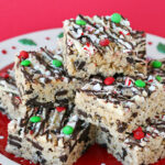 six rice krispie treats made with peppermint oreos and decorated with chocolate and sprinkles on a white plate with a red background.