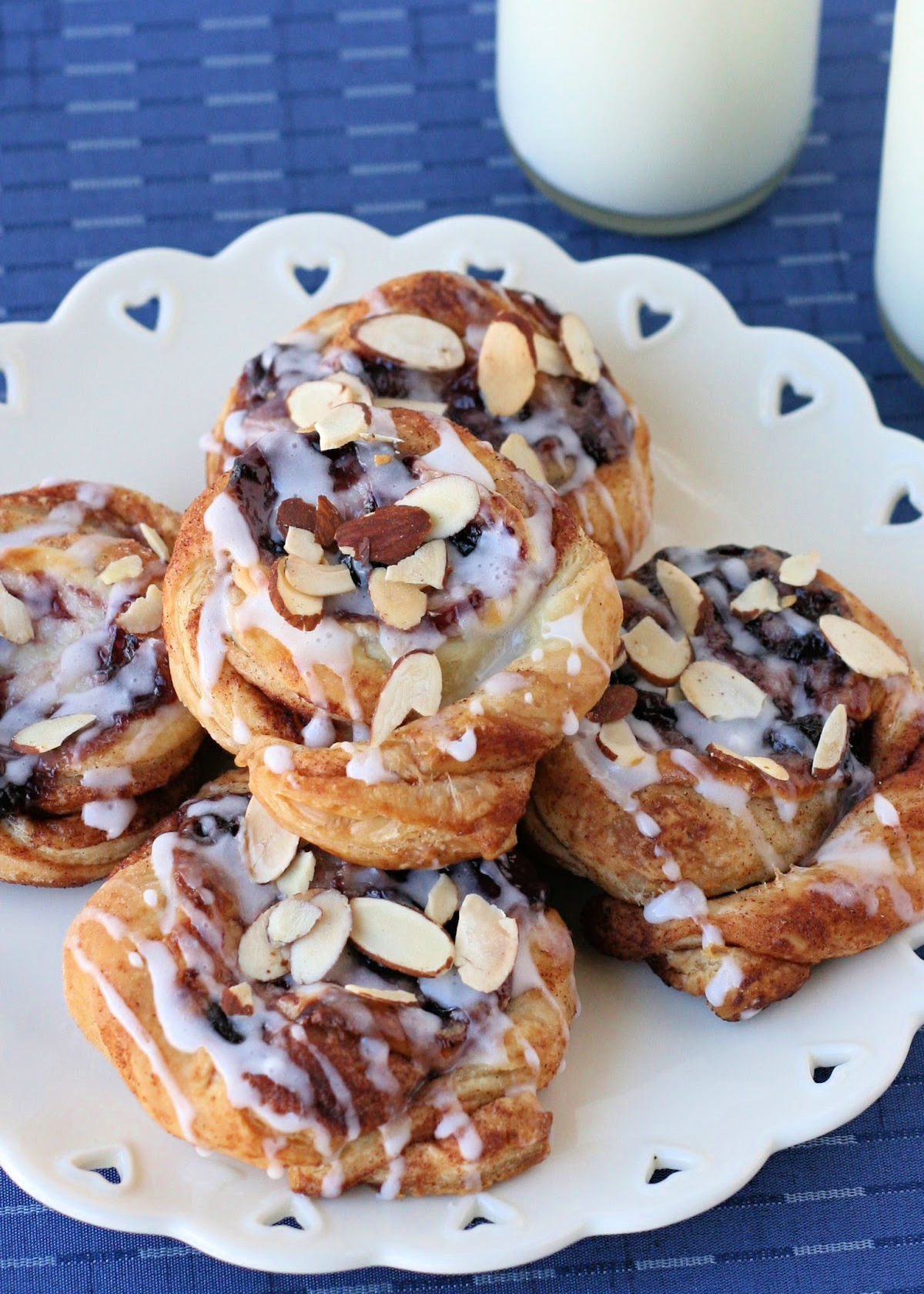 five cheesecake danishes made with blueberry jam sitting on a white plate with a heart scalloped edge.