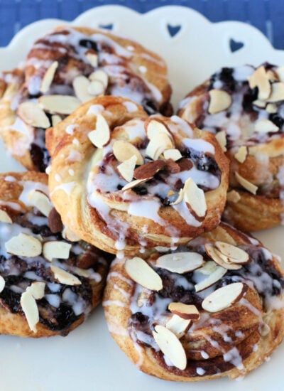 pastries made with puff pastry, cream cheese and blueberry jam drizzled with a glaze and sliced almonds sprinkled on top.