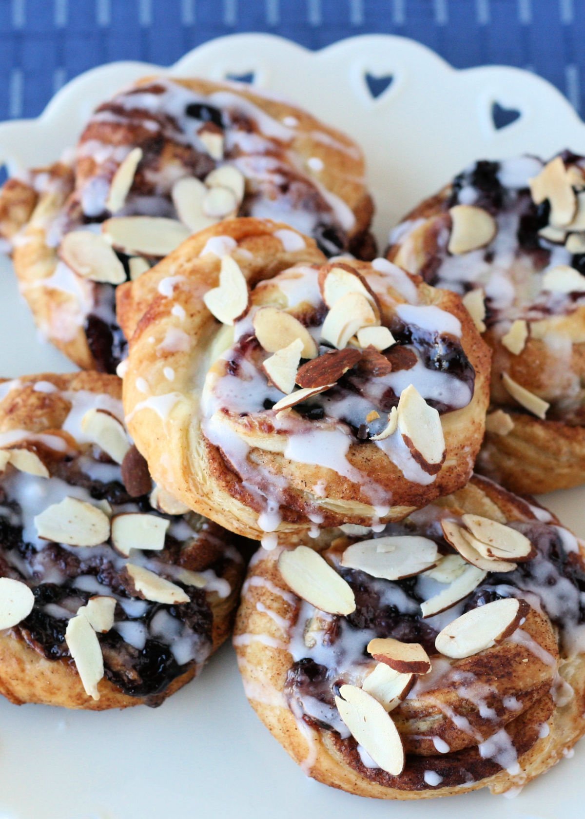 five cheesecake danishes made with blueberry jam sitting on a white plate with a heart scalloped edge.