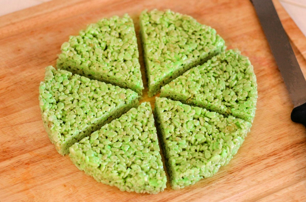 green rice krispie treats cut into six wedges sitting on wood cutting board.