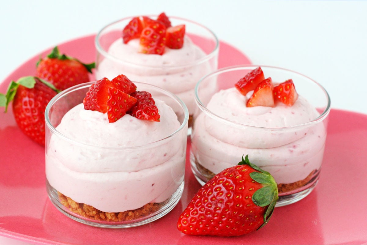 3 strawberry cheesecake mousse with graham cracker layer in small glass jars topped with fresh diced strawberries