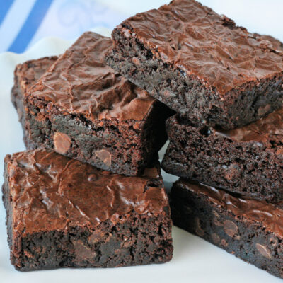 homemade brownies stacked on white plate with white and blue napkin in background.