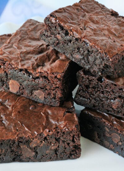 homemade brownies stacked on white plate with white and blue napkin in background.