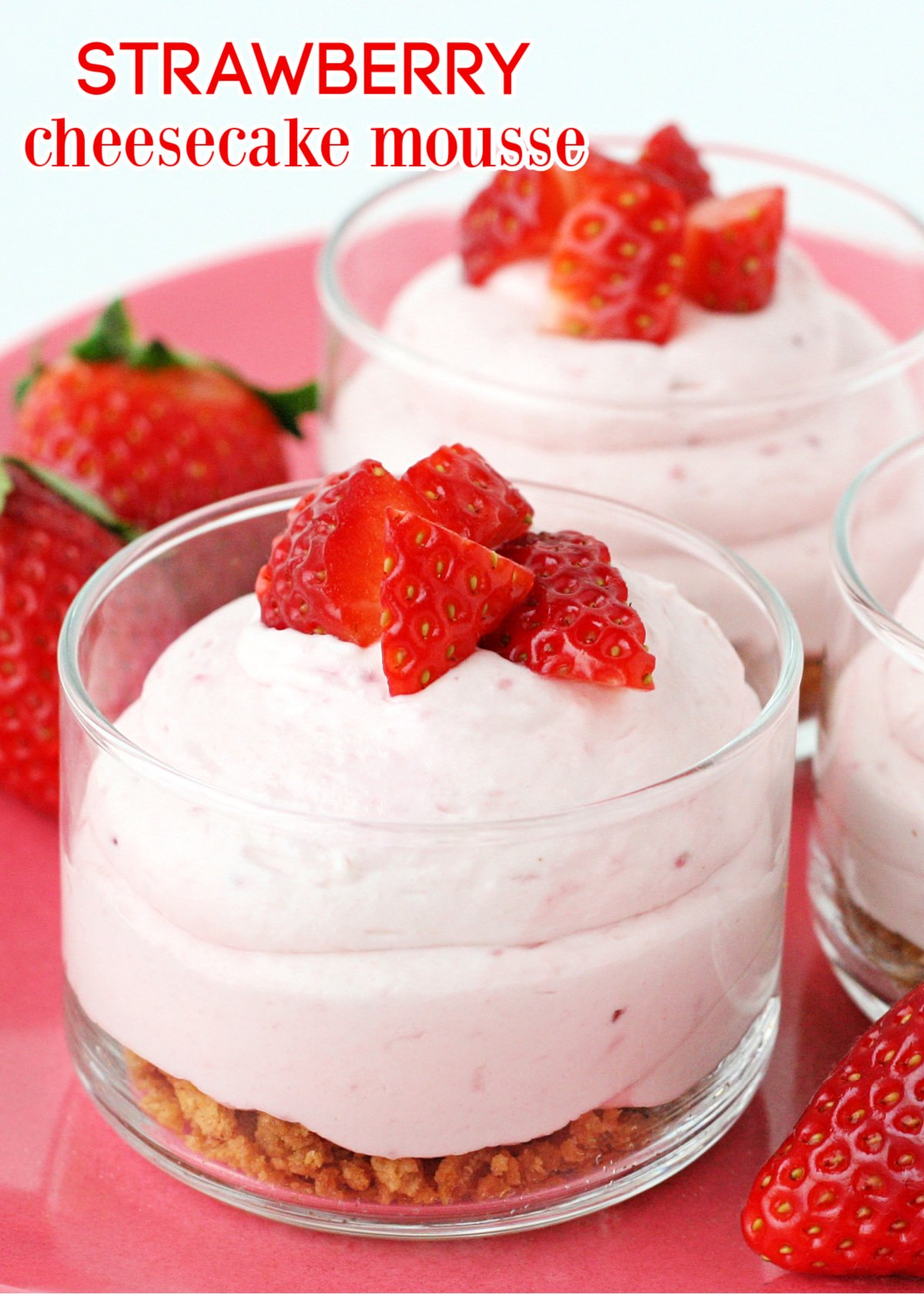 strawberry cheesecake mousse with graham cracker layer in small glass jar topped with fresh diced strawberries and text overlay