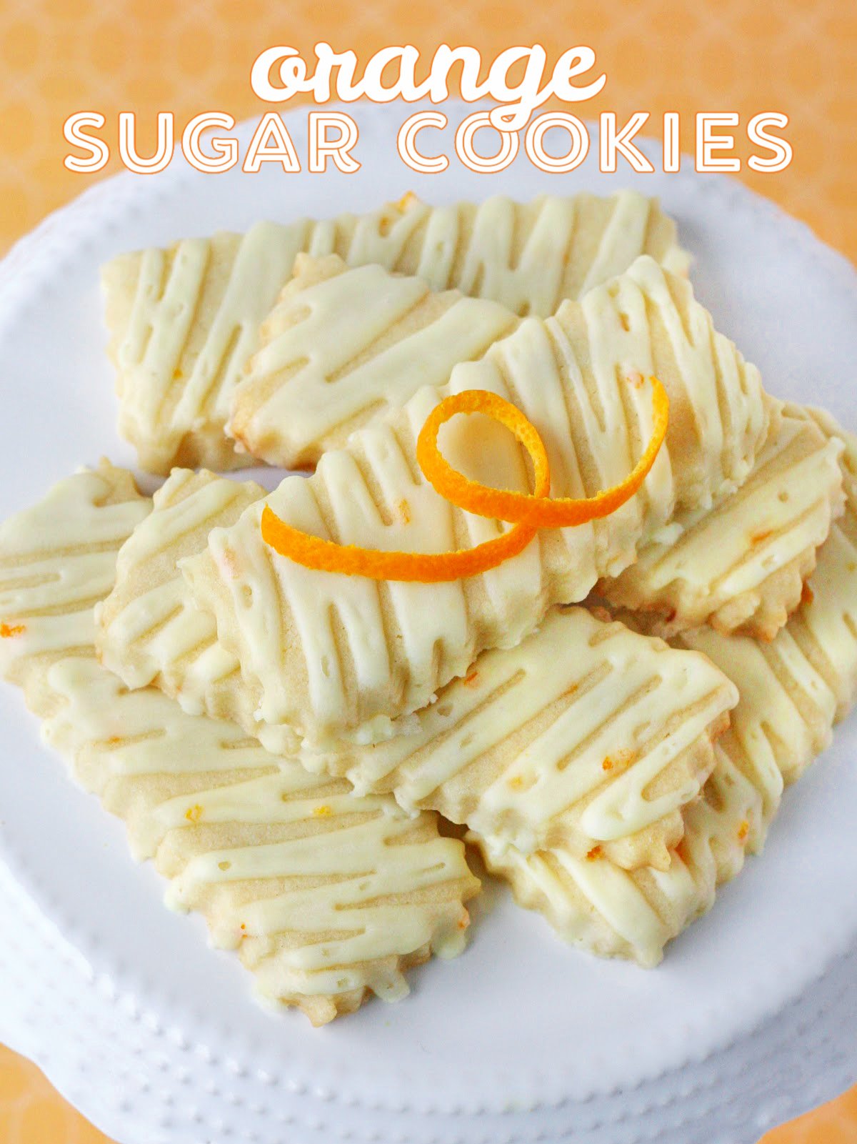 orange sugar cookies on white cake stand with title overlay at top of image.