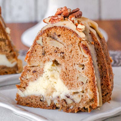 slice of apple bundt cake on a white square plate. you can see the cheesecake filling and praline frosting on top of the cake.