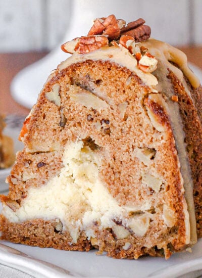 slice of apple bundt cake on a white square plate. you can see the cheesecake filling and praline frosting on top of the cake.