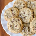 chocolate chip cookies piled on white cake stand with wood surface underneath square image