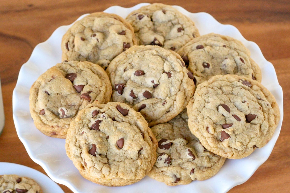 chewy chocolate chip cookies piled on white cake stand on wood surface