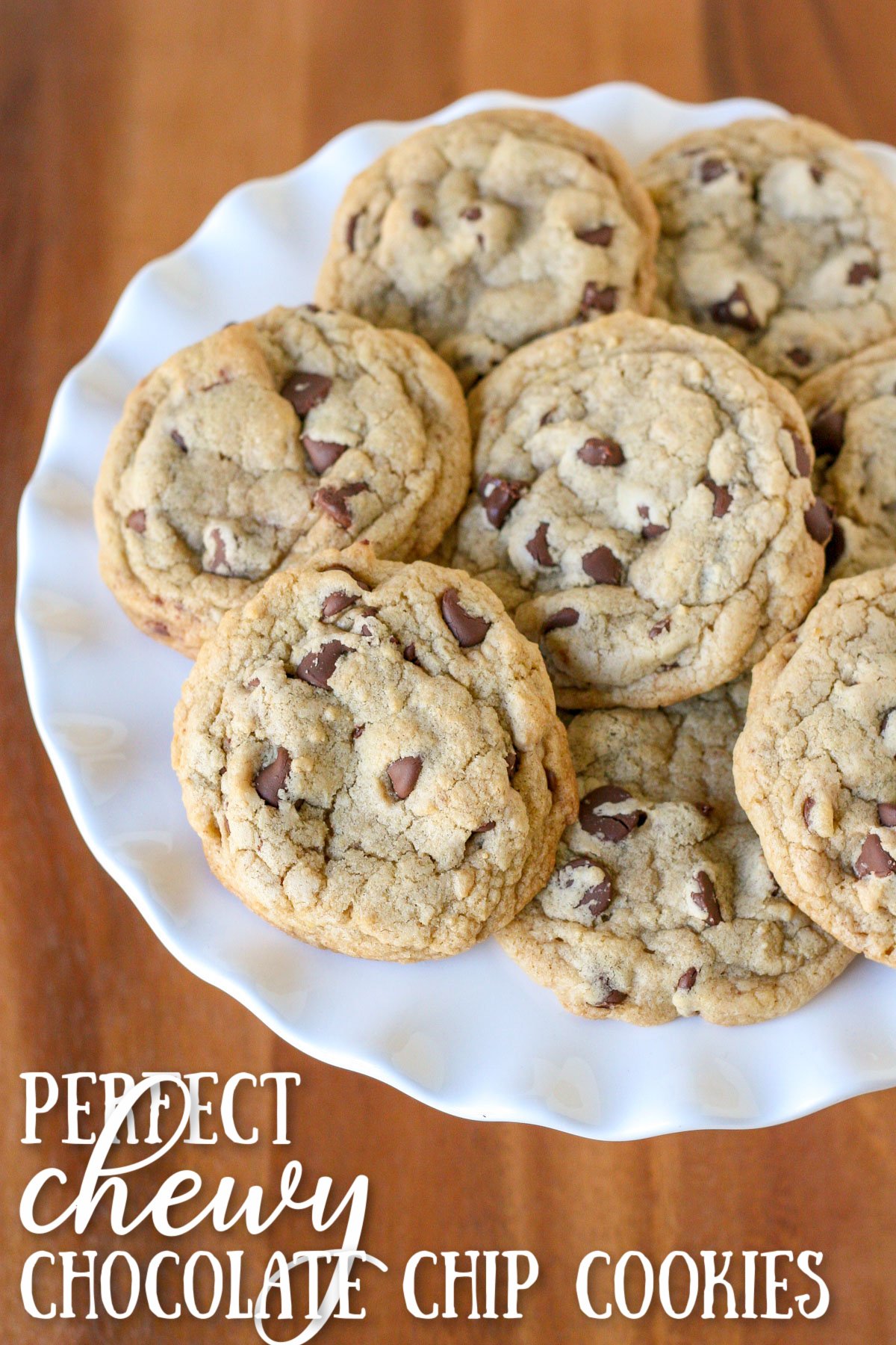 chocolate chip cookies piled on white cake stand with wood surface underneath and text overlay at the bottom