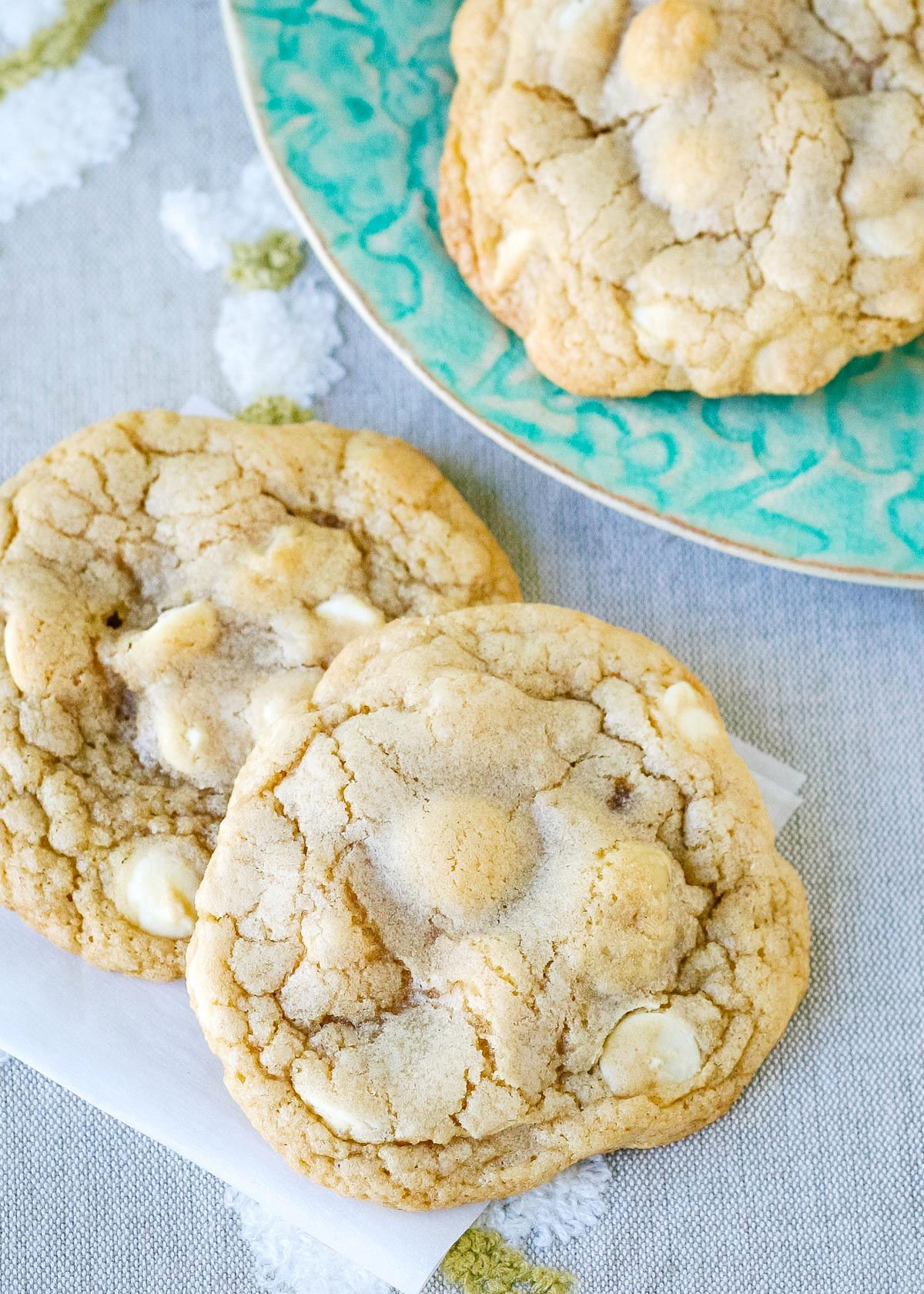 two cookies on piece of parchment and another cookie on a plate behind 