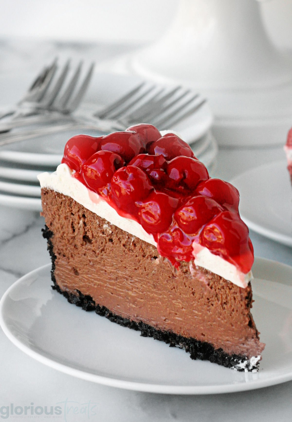 generous sized slice of black forest cheesecake sitting on white round plate with more plates in the background.